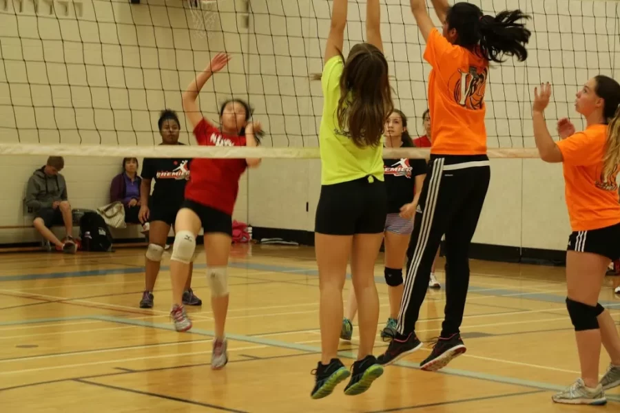 Girls jumping to block a volleyball spike during a game, showcasing teamwork and athleticism.